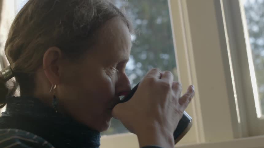 A woman drinking from a mug next to windows