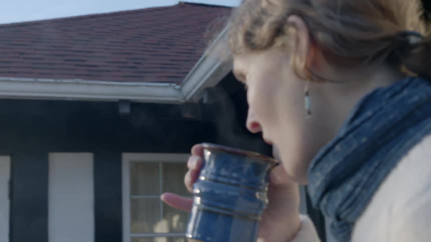 A woman is standing outside drinking from a mug