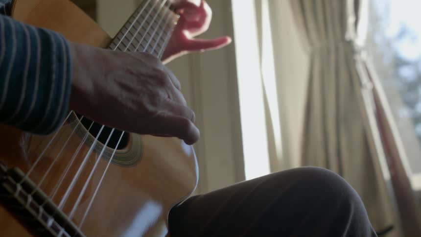 A man stands in front of a window and plays the guitar
