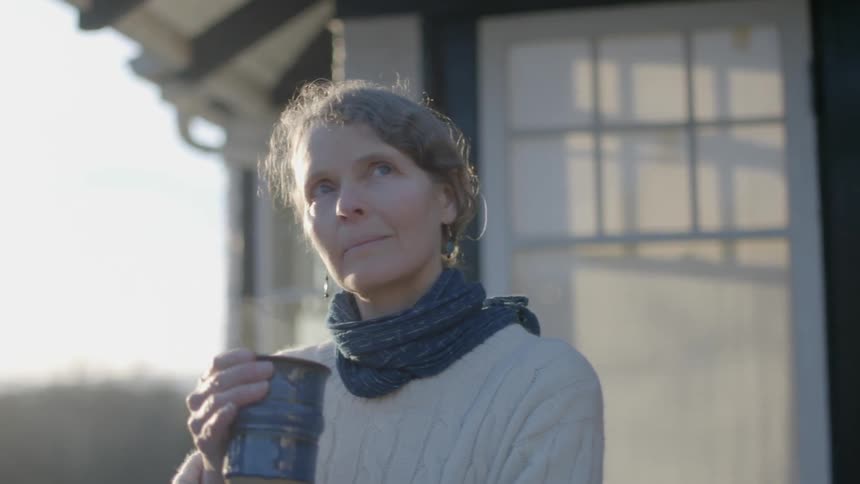 A woman stands outside her home with a steamy mug