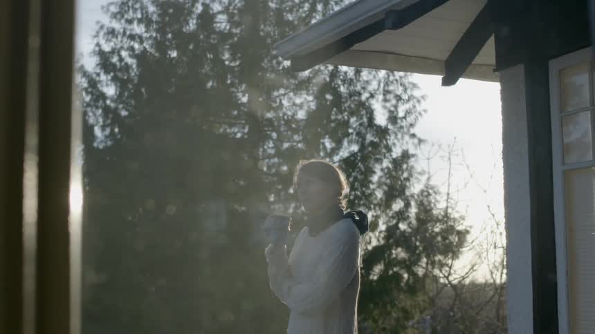 A woman stands outside holding a steaming mug