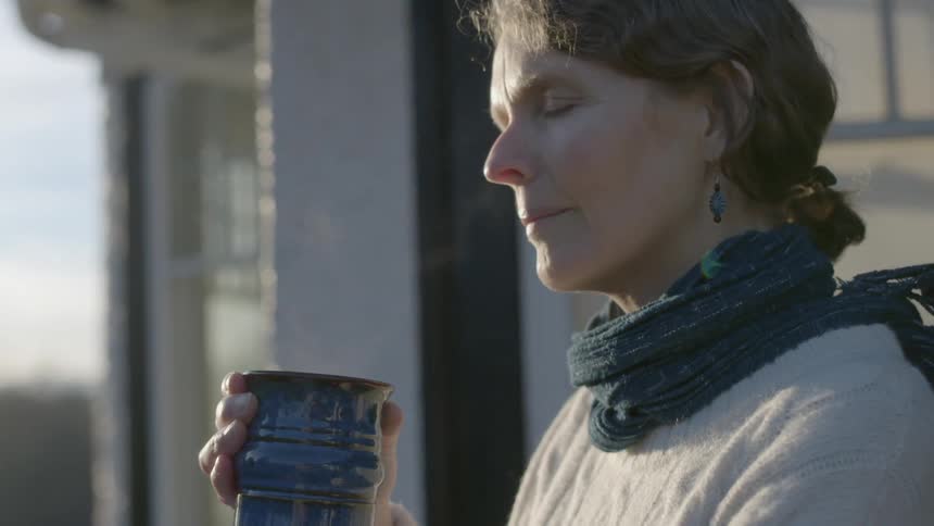 A woman holding a steaming cup of liquid while she is outdoors