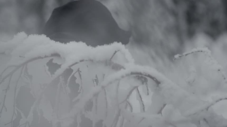 A person wearing black robes is walking past a snow covered area