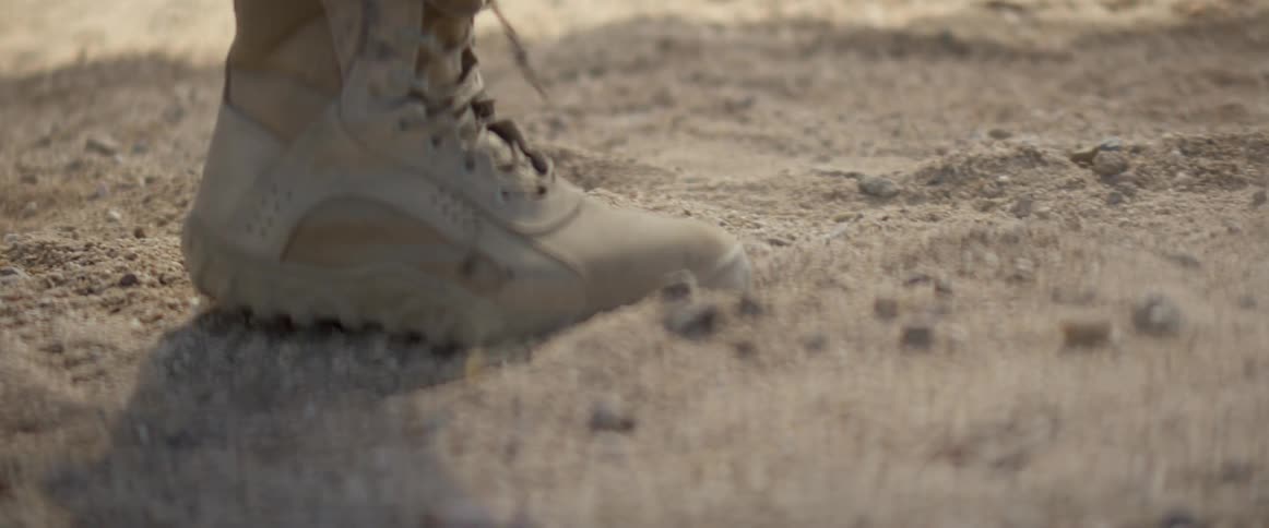 A person wearing tan hiking boots struggles to walk through sand