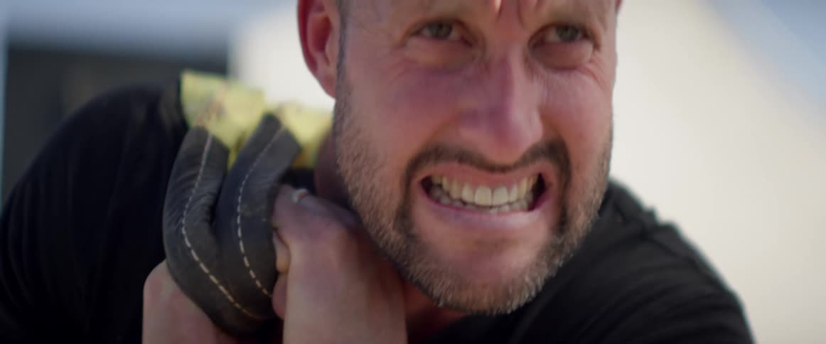 Man grimaces as he carries something heavy over his shoulder
