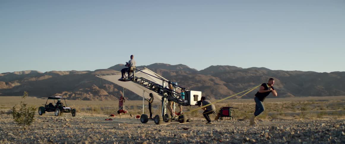 A man uses rope to pull a man sitting on a crane as people around them film the scene