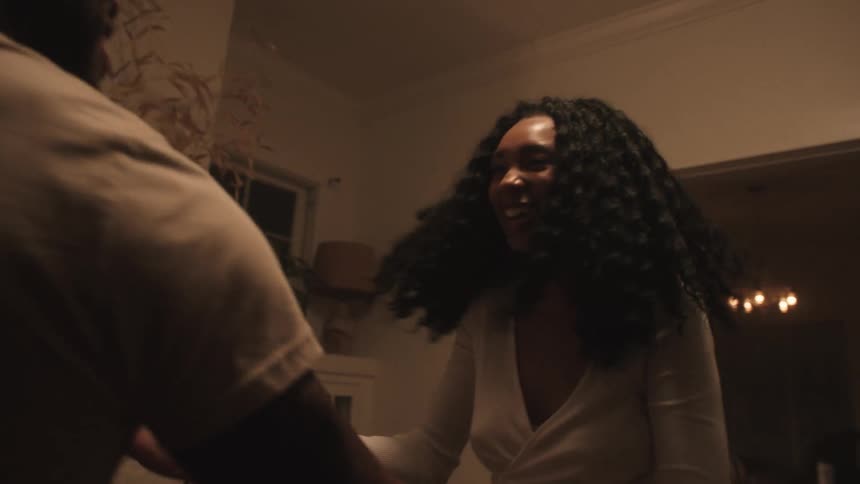 A black woman and black man dance in the living room of a house