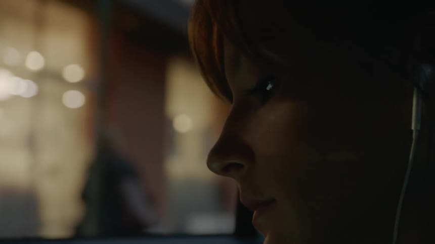 A woman with earbuds in a vehicle and out the window showing people walking on the street