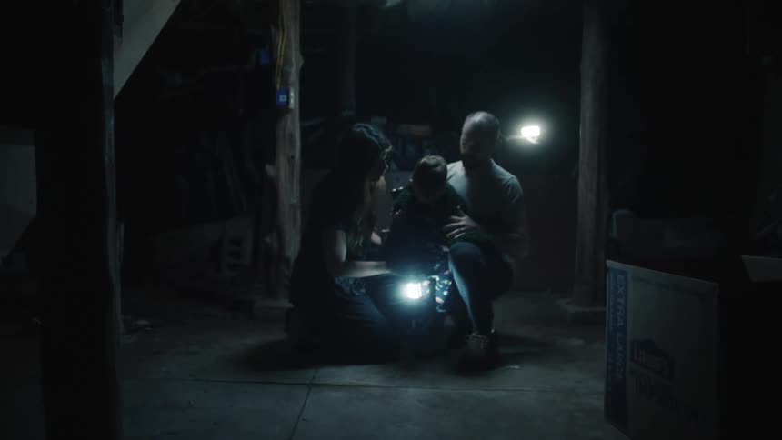 A mother and father comfort a small boy in a dark basement