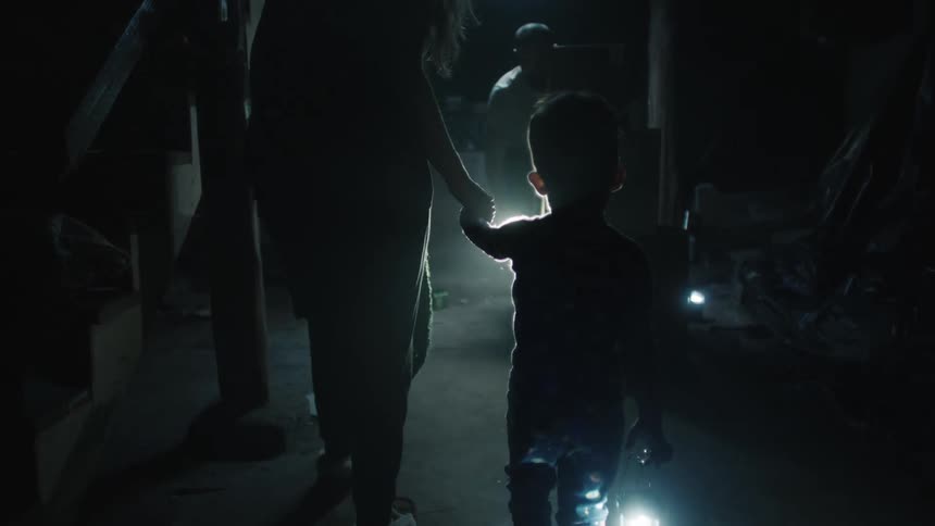 A woman holds a toddlers hand walking through a dark room with flashlights