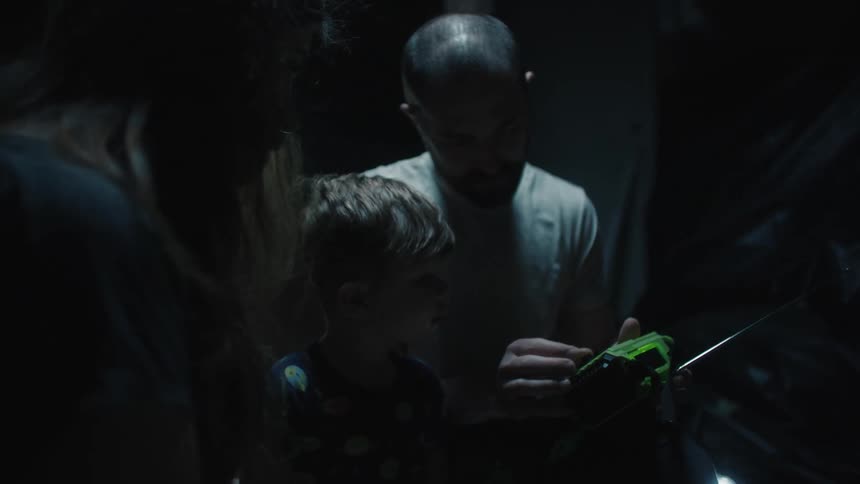 A white woman white man stand outdoors at night with a child while using a radio