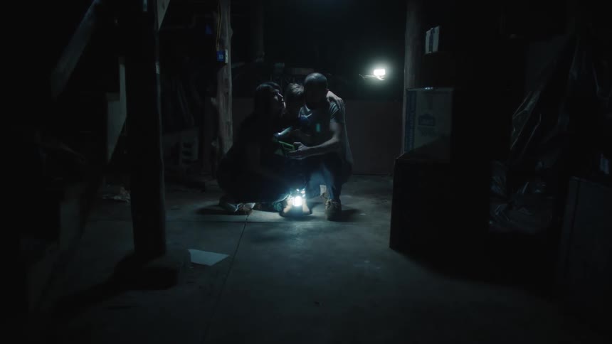 A family cuddles together in the basement and use lanterns and a flashlight