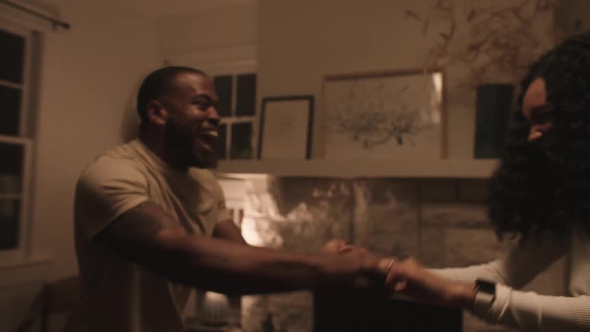 A husband and wife laugh as they dance around their living room