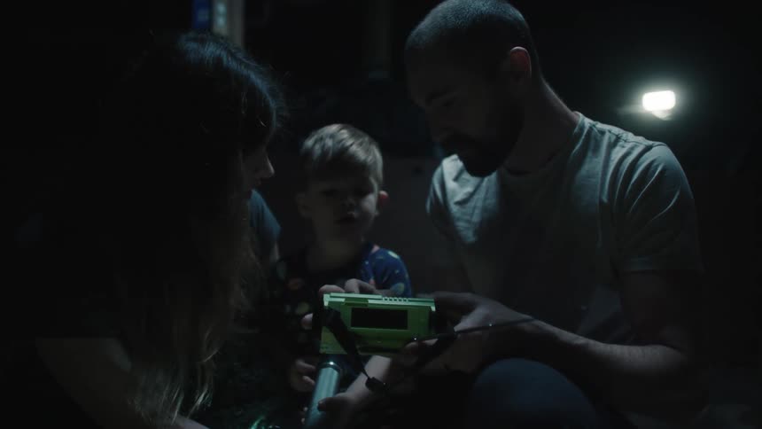 A family sits outside in the dark with a flashlight and listens to a radio