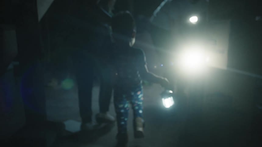 A young child holding a lamp walks with an adult outdoors at night
