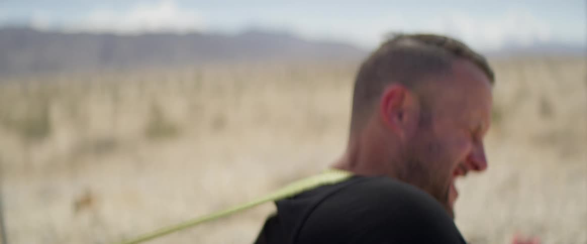 A man pulling something with a strap with mountains in the background