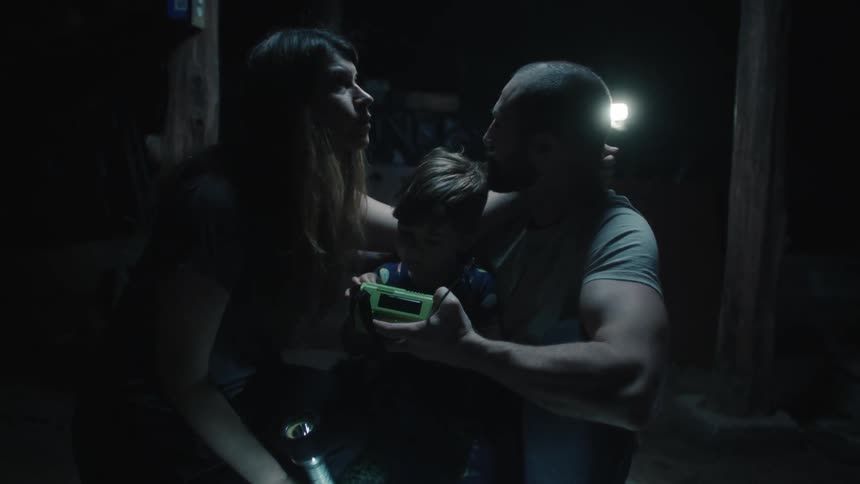 A husband wife crouched on either side of their young son as they anxiously wait in a storm cellar