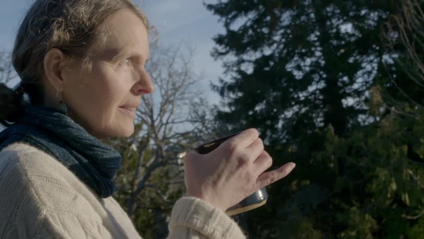 A woman sips from a mug as she stands outside