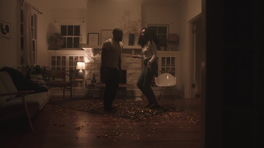 A black woman and black man dance in the living room of a home