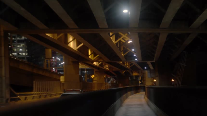Cars travel under an elevated roadway in a city at night