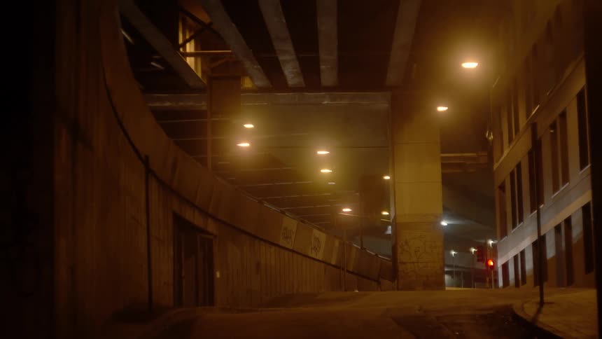 An alley between a building and a parking garage is dimly lit at night