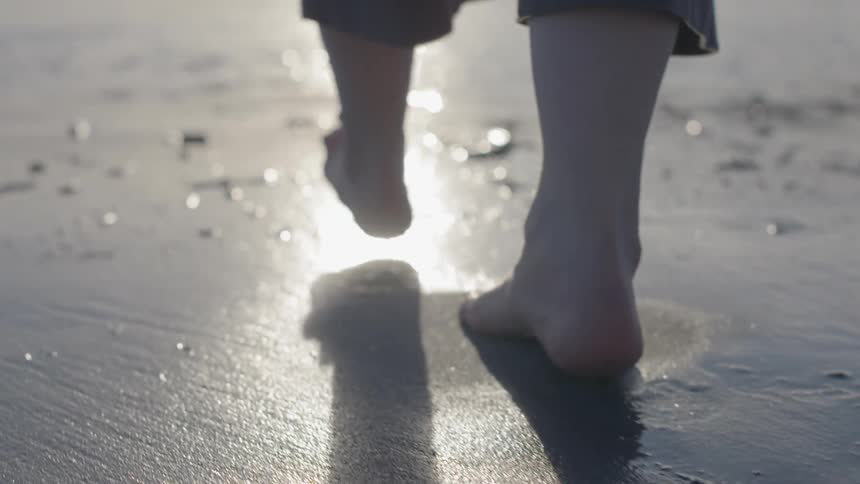 Feet walking across wet sand towards a body of water