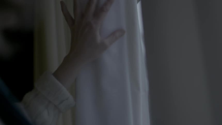 A woman caresses the fabric of a window