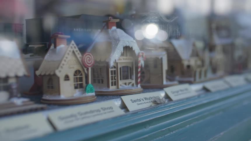 Labeled miniature houses stand displayed in large paneled window