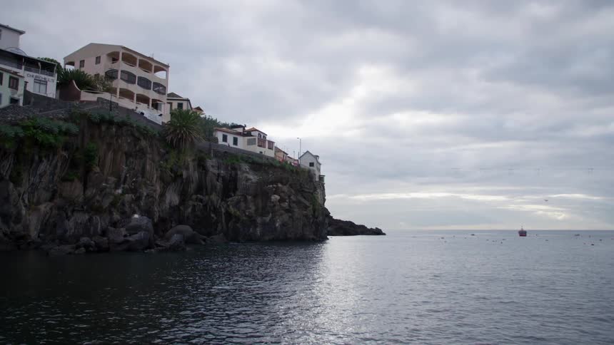 Buildings crowd cliff edge as rippling water reflects light from cloudy sky