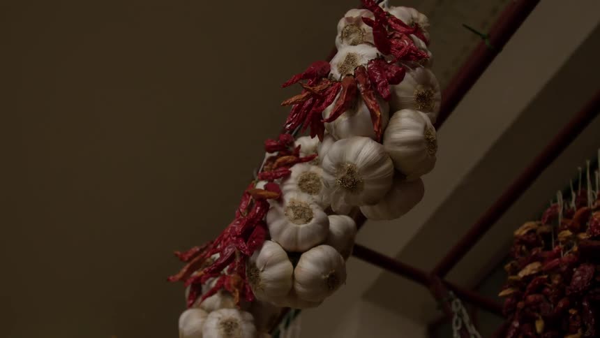 Strands of garlic and dried chili peppers hang on bars against earth tone walls and ceiling