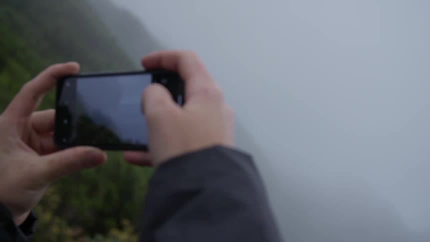 Man takes a photograph of foggy mountains and a valley with his smartphone
