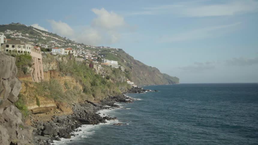 Waves crash against cliff under city occupying mountain top