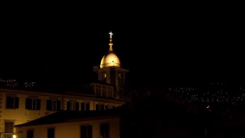 A church with a lighted dome with a cross on top at night