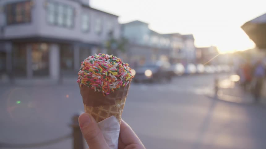 A person stands on the corner of a town holding an ice cream cone