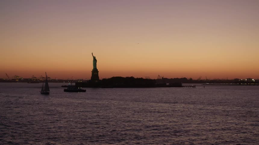 Statue of liberty shows as silhouette against orange sky