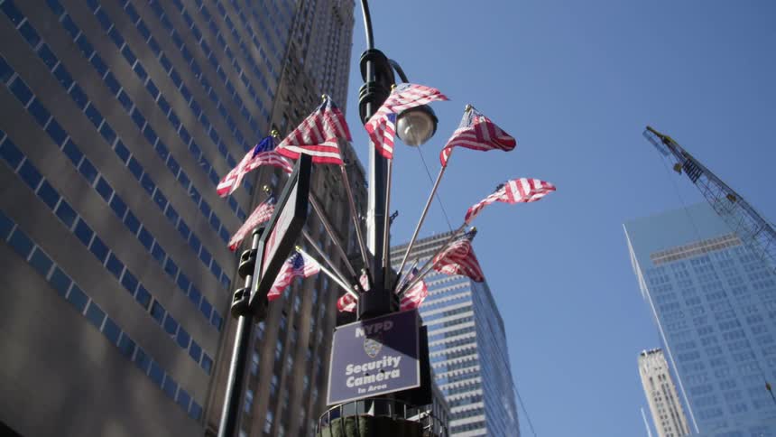 American flags waving on a light post with buildings in the background