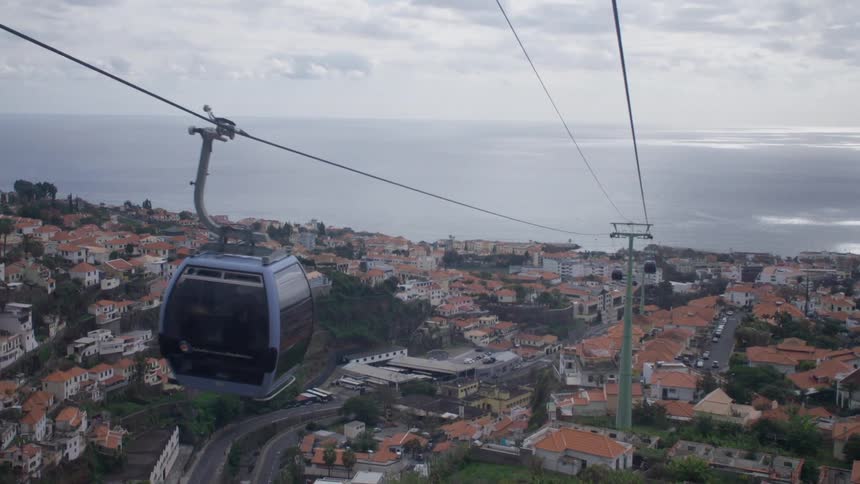 Overhead cable car passes over road meandering through red roofed town
