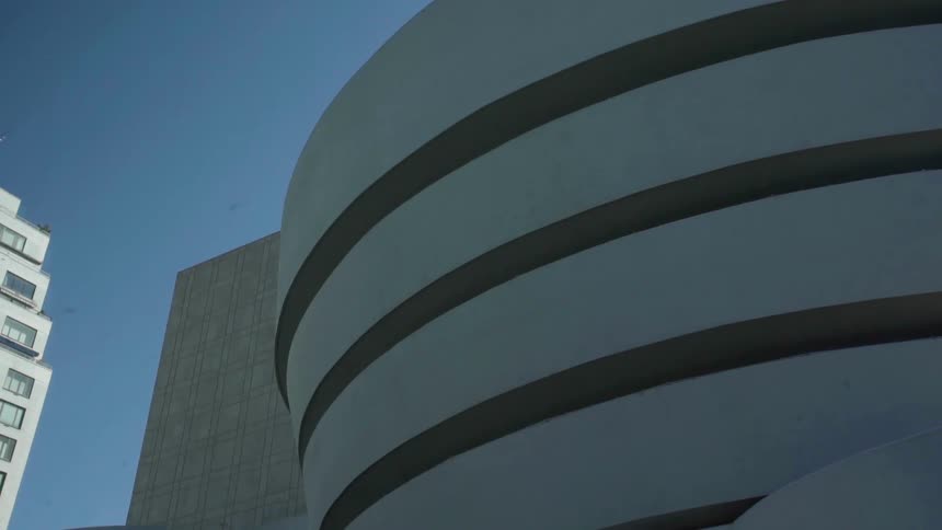 Circular top floors of parking garage stands among other buildings under blue sky