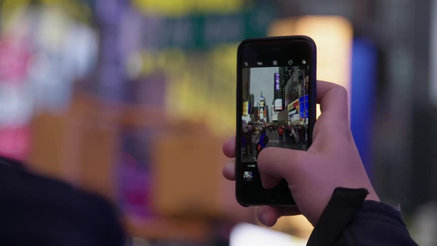 A person holding up a phone filming a city scene with pedestrians and buildings