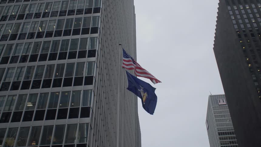 Flags wave in breeze on flagpole near skyscrapers