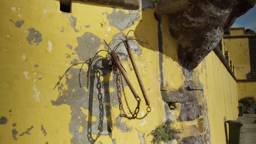 Grappling hook hangs on yellow wall coated in plaster near alley
