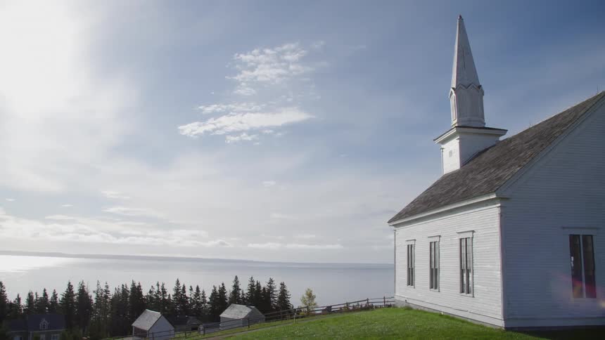 Little white church with a steeple sitting on a hill overlooking the ocean