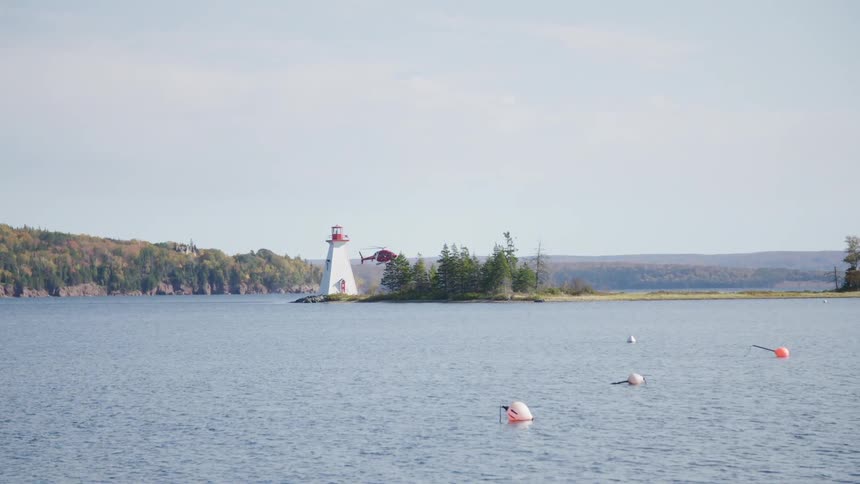 A helicopter flies over the water and behind a lighthouse