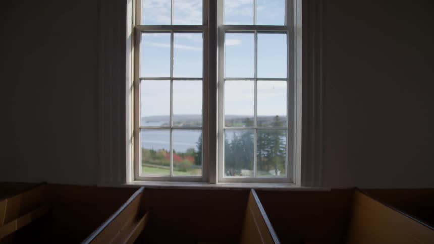 A window in a church overlooking a field that leads to the ocean