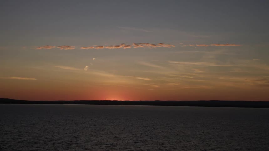 Sun rises on the horizon over shore bordering ocean