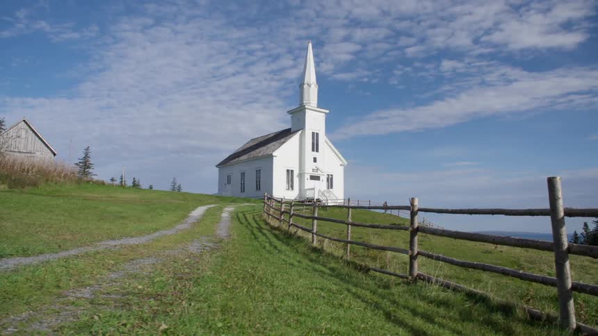 A pretty white church at the end of a dirt and grass road with grass fields on a bright blue sky day