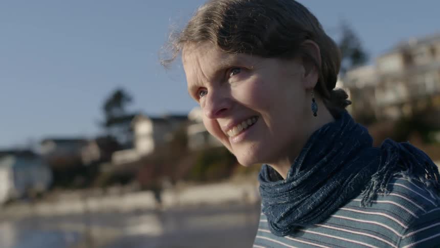 An older woman standing on a beach smiling