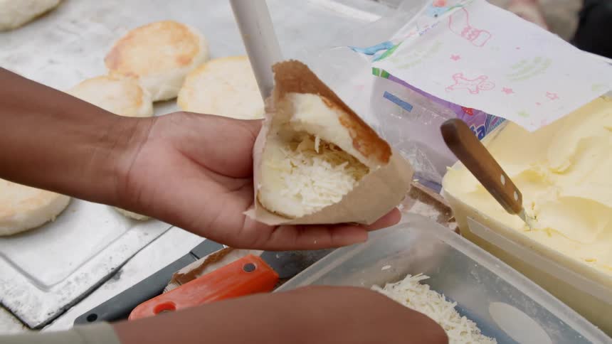 A person is stuffing shredded cheese into a roll