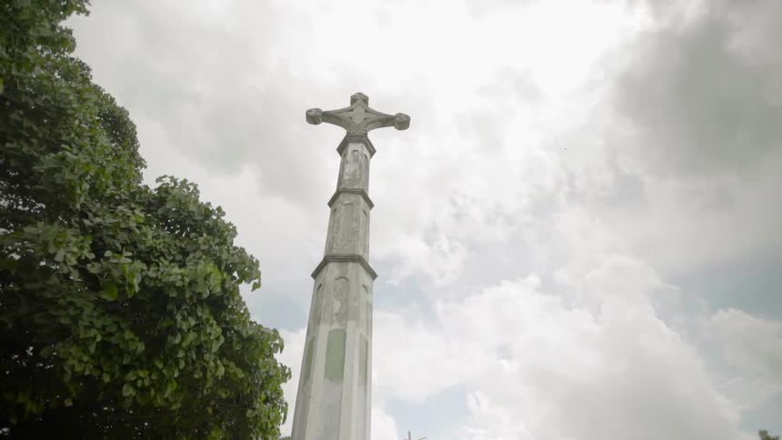 A stone pillar with a cross on top with the sky above