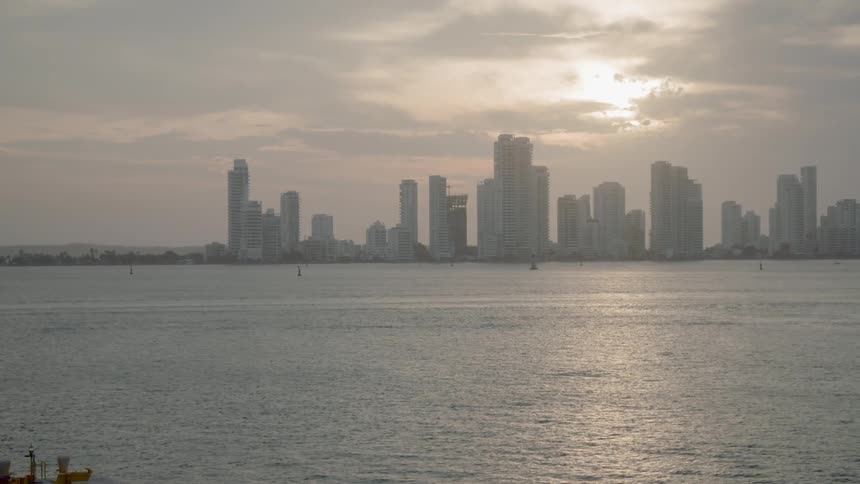 View of skyline with sea in front of skyscrapers and the sun shining through the clouds